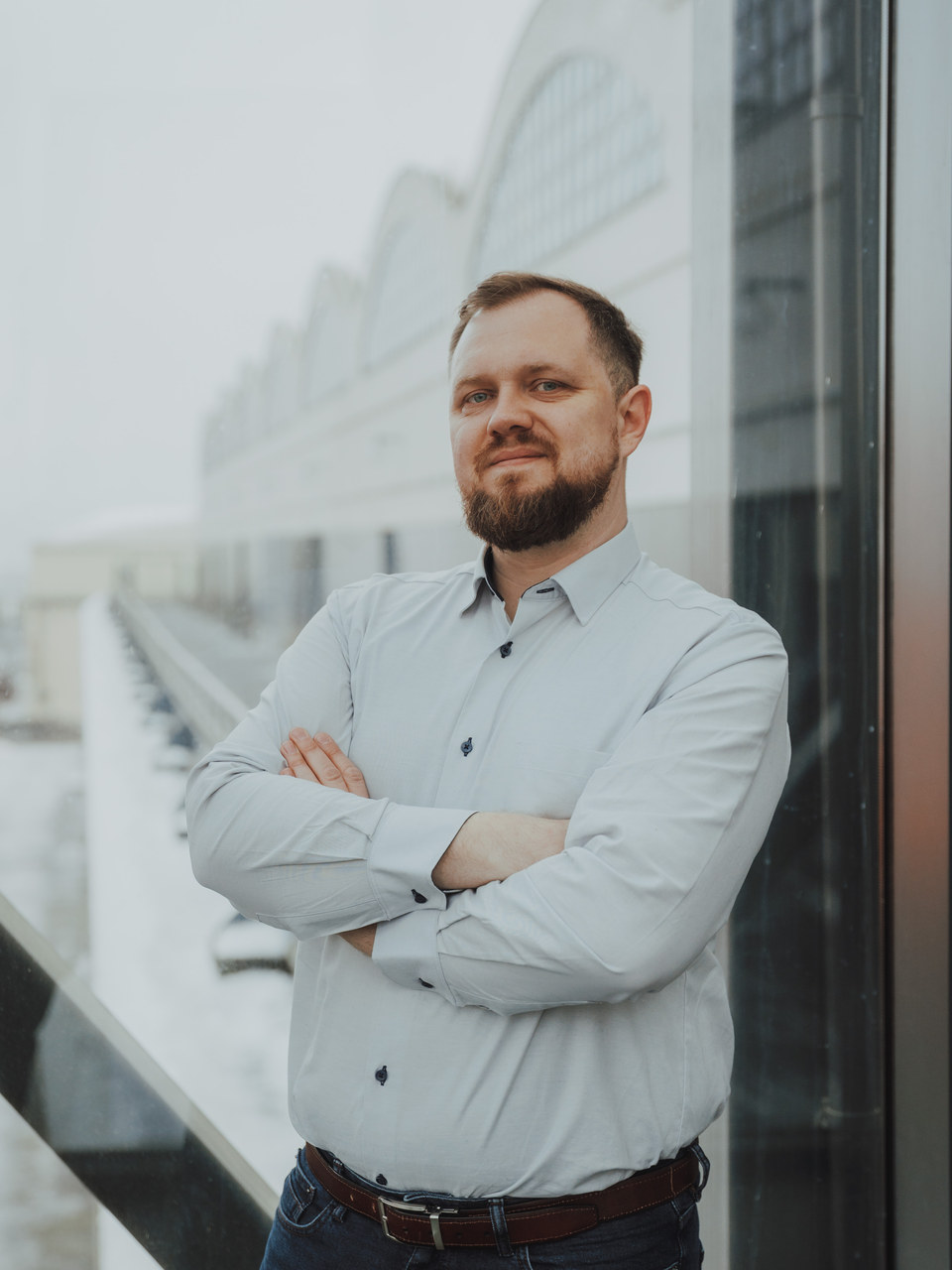 Łukasz Stocki w jasnej koszuli, ręce skrzyżowane, przed przeszkloną elewacją
