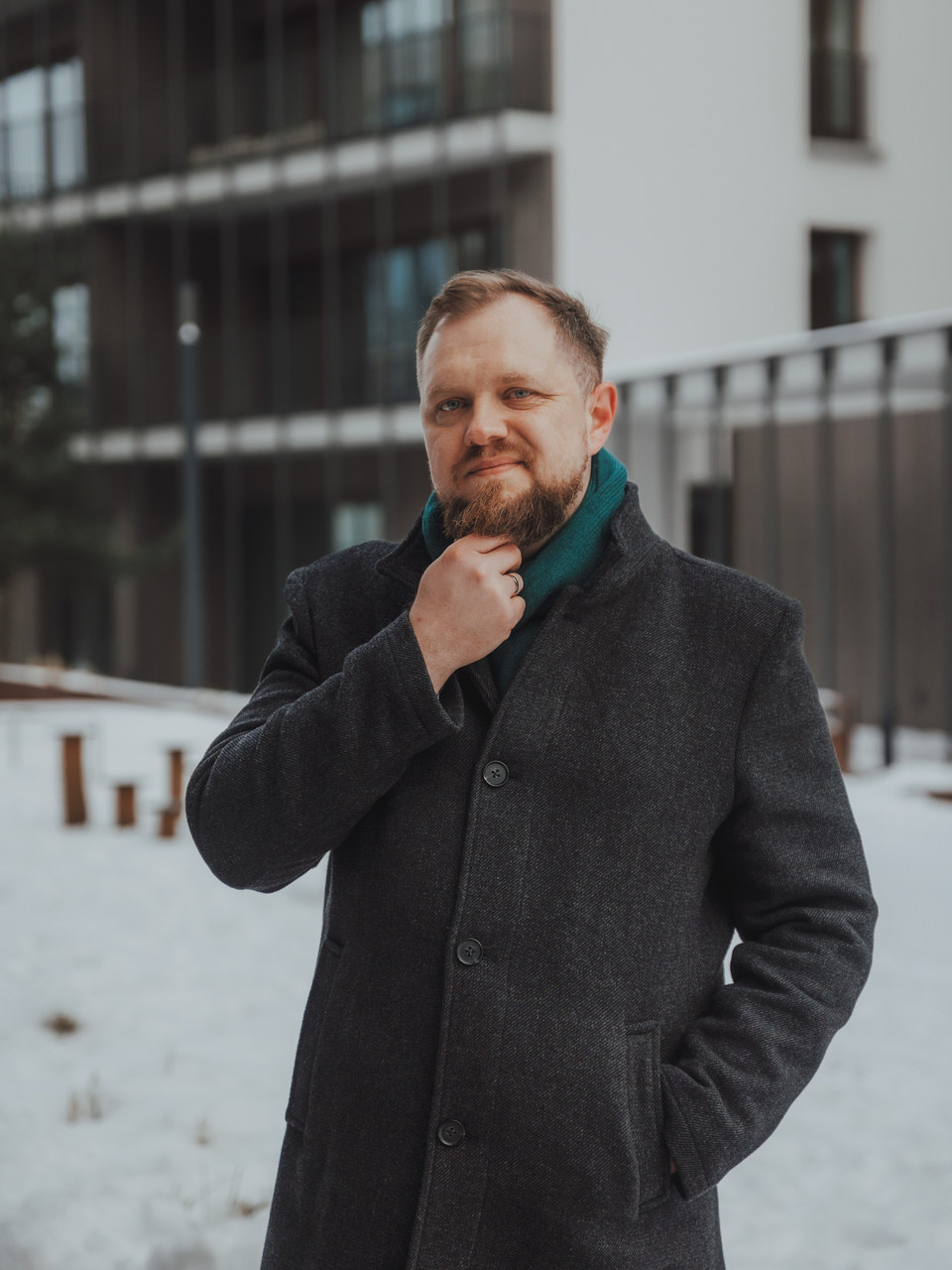 Łukasz Stocki w ciemnym wełnianym płaszczu z turkusowym szalikiem, lekki uśmiech